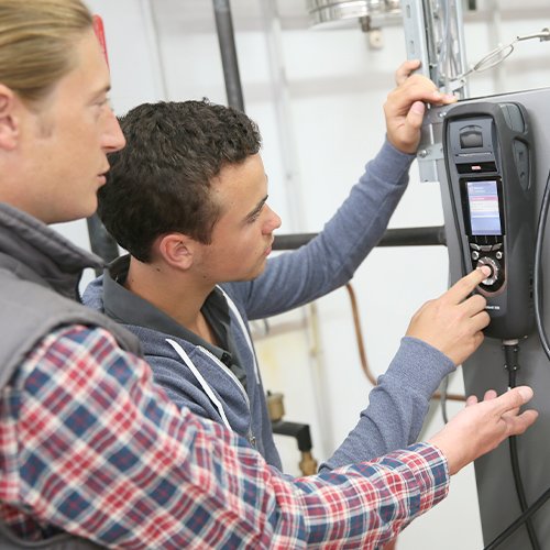 Zwei Anlagenmechaniker die mit einem Klimamessgerät eine Heizung prüfen