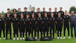 Die Fußballmannschaft posiert auf einer Wiese, alle tragen schwarze Sportkleidung und zeigen stolz ihre Teamidentität.