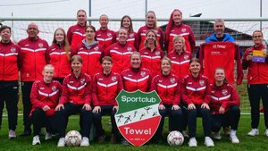 Die Spielerinnen des SC Tewel stehen zusammen, lächeln und zeigen ihre Teamkleidung, während sie eine Dankeskarte präsentieren.
