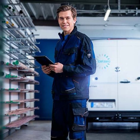 Ein junger Mann in Arbeitskleidung hält ein Tablet in der Hand in einer Halle