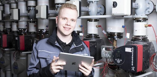 Ein junger Anlagenmechaniker mit einem Tablet in der Hand vor einer Heizungsanlage