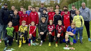 Die Mannschaft besteht aus Jungen und einem Mädchen, die in verschiedenen Trikots stehen und stolz ihre Teamgeist zeigen.