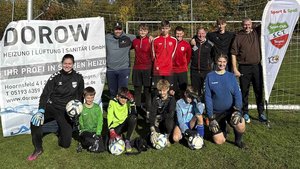 Die Mannschaft steht stolz vor einem Werbebanner, während die Torhüter in ihren Trikots mit Bällen in der Hand lächeln.