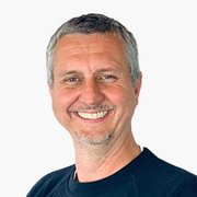 Der Mann hat ein freundliches Lächeln und trägt ein schwarzes Oberteil, während er direkt in die Kamera schaut.