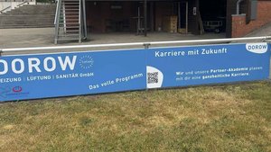 Ein großes Werbeschild von Dorow, das Dienstleistungen in Heizung, Lüftung und Sanitär anbietet, steht auf einem Platz.